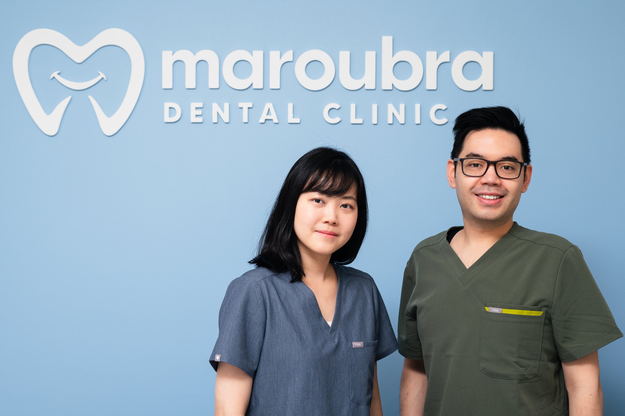 male and female in front of maroubra dental clinic sign